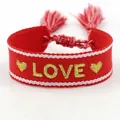 Detailed macro of red hand-woven friendship bracelet with gold LOVE embroidery and tassels - L011 LOVE / Red