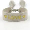 Detail of bohemian woven bracelet featuring golden LOVE embroidery and tassel accents - L012 LOVE / Light Gray