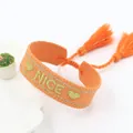 Detail van de oranje geweven armband met goud geborduurde NICE-letters en kwastjes - Oranje NICE-3 Stijl