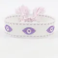 Detailed macro view of woven Evil Eye embroidery with soft lilac tassels and stitching - Evil Eye Purple