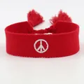 Dettaglio di un bracciale rosso intrecciato con simbolo della pace ricamato e nappe decorative - Segno della Pace Rosso