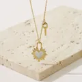 Collar dorado con colgante de corazón solar y piedra blanca sobre soporte de piedra - Dorado