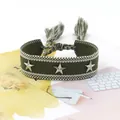 Detalle de pulsera tejida verde militar con estrellas y borlas sobre un libro - Verde Militar (13#)