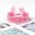 Détail du bracelet tissé rose avec clous en cœur argentés et breloques à pompons - Rose
