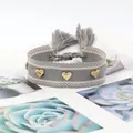 Close-up of woven heart bracelet with golden rivets and boho tassel detail - Gold Heart Rivets / Grey White Twill (H-G-017)