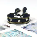 Détail d'un bracelet tissé main avec clous cœur argentés et motifs tissés noir et or - Noir & Or
