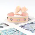 Détail d'un bracelet tissé rose et jaune orné de clous coeur argentés et de glands - Pink Yellow Tones
