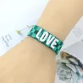 Green checkerboard woven bracelet featuring white LOVE embroidery and adjustable tassels - Size 8