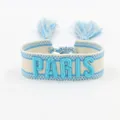 Detailed view of cream and sky blue woven friendship bracelet with PARIS embroidery and tassels - Blue PARIS Embroidery Tassel / Blue PARIS