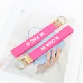 Detalle del llavero rosa bordado BE KIND con anilla dorada sobre un bolso azulado - Be Kind Estilo 1