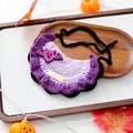 Detail van een paars gebreide Halloween-huisdier bandana met glittervleermuis en goud - Halloween Gouden Tag Gebreide Slab - Vleermuis