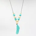 Gros plan sur le pendentif plume en silicone et les perles du collier de dentition - Bleu lac