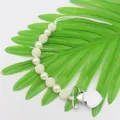 Detalle macro del sujetachupetes de perlas blancas con clip metálico de corazón - Blanco