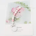 Silicone pacifier clip with pink and white beads on a floral background card - Pink