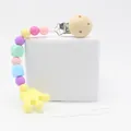 Silicone pacifier clip with macaron beads and a yellow crown charm on a white stage - Wood Color