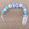 Nahaufnahme von Schnullerkette mit blauen Silikonperlen und Cartoon-Anhänger auf Holzboden - Waschbär - Blau