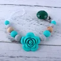 Mint green silicone pacifier clip with rose bead and marble accents on wood background - Lake Blue