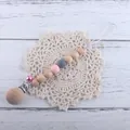 Detailed shot of beech wood and silicone pacifier clip with a pink bell and lace mat - Pink Pacifier Clip