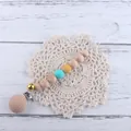 Detail of beech wood and silicone pacifier clip with golden bell on lace mat - Lake Blue Pacifier Clip