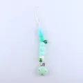Silicone baby pacifier clip with blue and green beads and metal bells on white background - Green