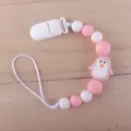 Pink silicone baby pacifier clip with cartoon penguin bead on a wooden surface - Penguin Pink