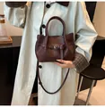 Detalle de bolso tipo cubo trenzado marrón oscuro con hebilla metálica y bandolera - Marrón