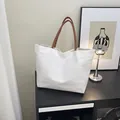 Bolso tote minimalista de lona blanca con asas de cuero marrón sobre un mueble moderno - Lona Blanca Con Asas Marrones / Blanco