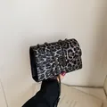 Detalle de bolso leopardo con tachuelas plateadas y cadena de metal sobre blanco - Negro