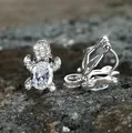 Macro shot of silver turtle clip-on earrings with sparkling zircon stones on a grey rock - White