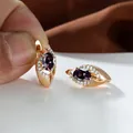 Dettaglio di orecchini dorati con gemma viola ovale e piccoli cristalli bianchi - Viola