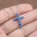 Mano che tiene una collana d'argento con elegante ciondolo a croce in zirconi blu - Blu