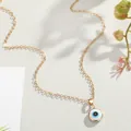 Macro shot of gold Evil Eye pendant necklace with blue enamel on a natural leaf background - White