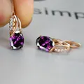 Macro view of rose gold huggie earrings with oval purple zircon and white crystal accents - Champagne Gold Purple Stone