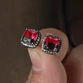 Macro view of square halo stud earring with red gemstone and micro-pave crystals - Black Gold Red Green
