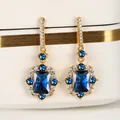 Elegante gouden oorbellen met een grote rechthoekige blauwe edelsteen en kristalaccenten - Goud Koningsblauw