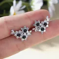Silver flower stud earrings with black gemstones and clear zircons held on a finger - Black Zirconia