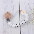 Detail view of baby pacifier clip with silicone daisy flower and wood beads on wood background - White