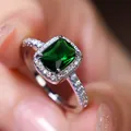 Emerald cut green crystal ring with halo setting and silver band on female hand - Size 5 / Platinum Plated Green Zirconia