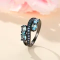Macro detail of bypass ring with light blue oval stones and dark blue accents on black band - US 6 / Black Gold Aqua Blue