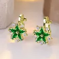 Elegant gold flower ear clips with green petals and white zircons on beige bokeh background - Gold Base Emerald Stone