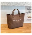 Detailaufnahme der dunkelbraunen Totebag mit weißer Aufschrift auf strukturierter Fläche - Braun