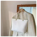 White snake-textured tote bag with gold chain strap on a stylish tweed coat - White