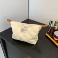 Elegante bolso de mano beige acolchado con cremallera dorada en mesa de madera - Blanco Roto