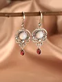 Detailed view of vintage silver hollow earrings with red stones on a wooden branch - Hollow Vintage Dangle / Antique Silver