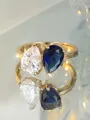 Detalle macro de un anillo dorado con circonitas pera azul y blanca sobre un espejo - US 6 / Blanco+Azul Real