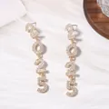 Detalle de pendientes dorados 2025 con pedrería brillante sobre fondo blanco suave - Estilo de Número 2025 / Oro Circonita Blanca