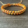 Detalle macro de cuentas de piedra natural de 6mm en una pulsera tejida ajustable - Naranja