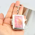 Book-shaped metal keychain with pink marble texture and silver hardware in hand - Rectangle Pink Marble