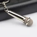 Polished silver microphone keychain with realistic metal mesh head on a dark leather surface - Silver