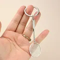 Miniature silver badminton racket keychain held in hand to demonstrate realistic sports design - Badminton Racket Pendant with Ring (A-003)